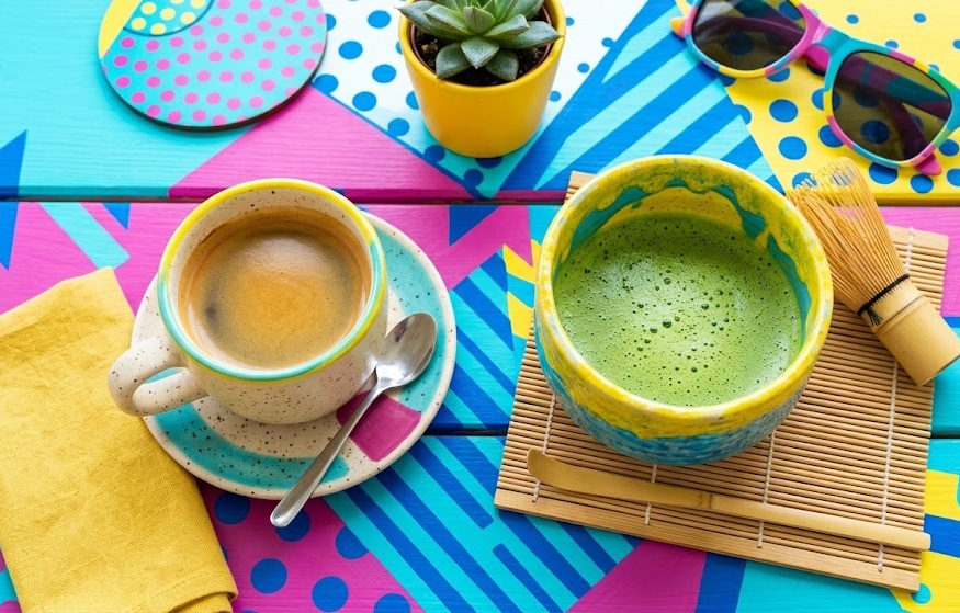 Una taza de café y un cuenco de matcha sobre una superficie de colores vivos